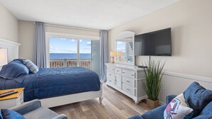 Une chambre avec un grand lit, une commode, une télévision et une vue sur la mer.
