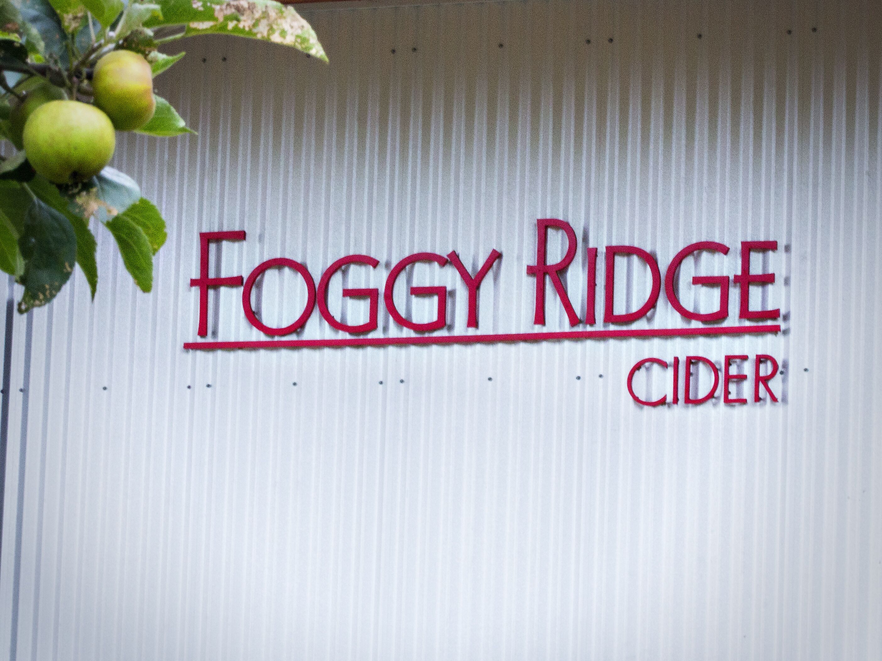 Una pared de metal corrugado con el texto 'Foggy Ridge Cider' en letras rojas.