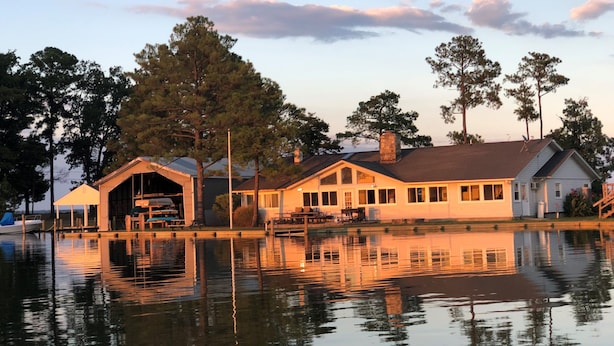 A lakeside hotel with a dock, a covered outdoor seating area, and a reflection in the water.