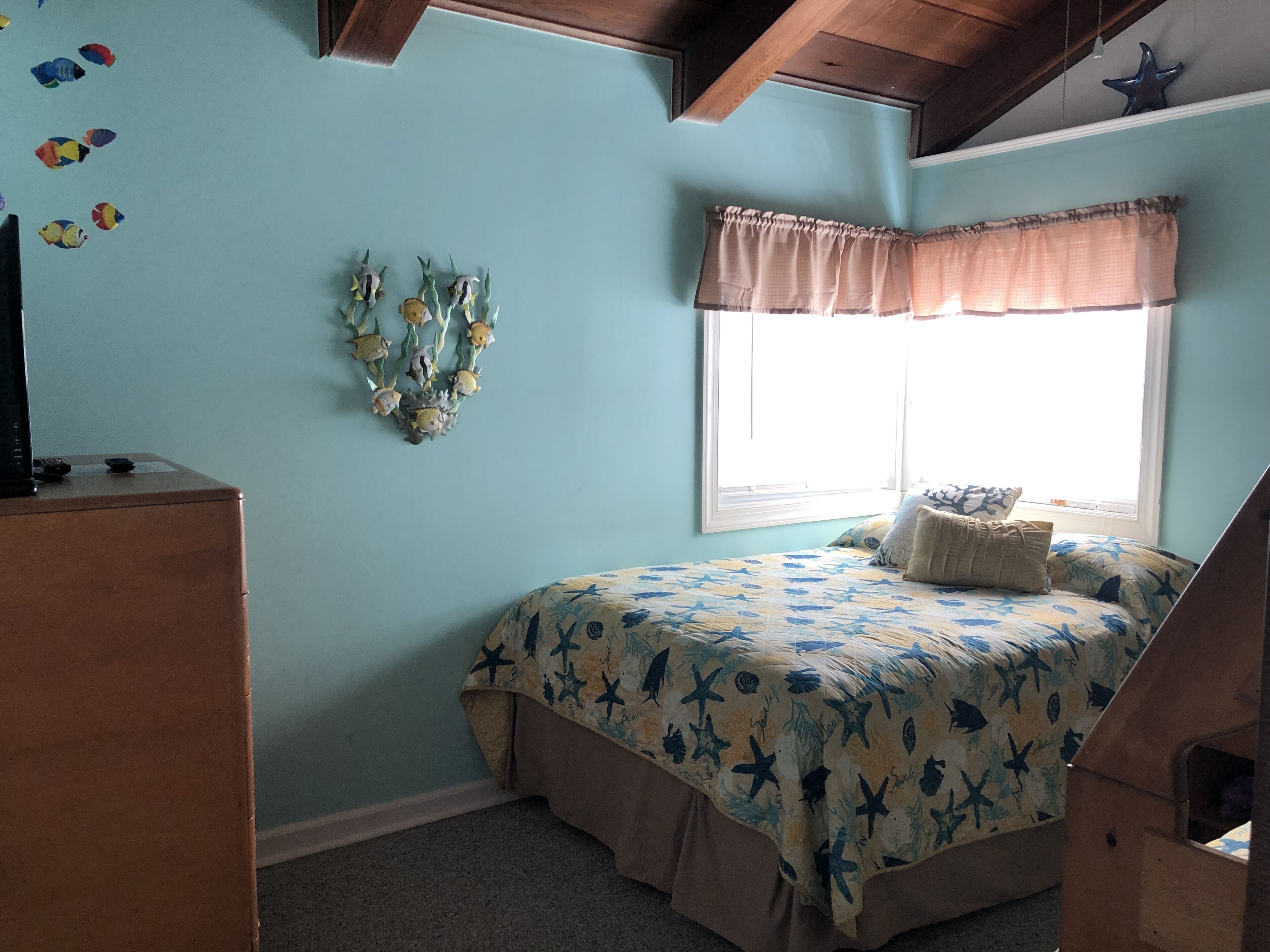 A bedroom with a bed, a dresser, a window with curtains, and a wall decoration.