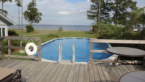 A wooden deck with a swimming pool, a hot tub, and a table.