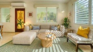 Una sala de estar con sofá, reposapiés, mesa de centro, una mesita auxiliar y una planta en maceta.