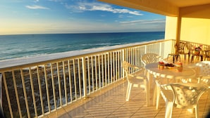 A balcony with a view of the ocean, white plastic chairs, and a table with decorative items.
