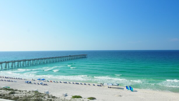 A beach with a pier extending into the ocean, sandy beach, and umbrellas.