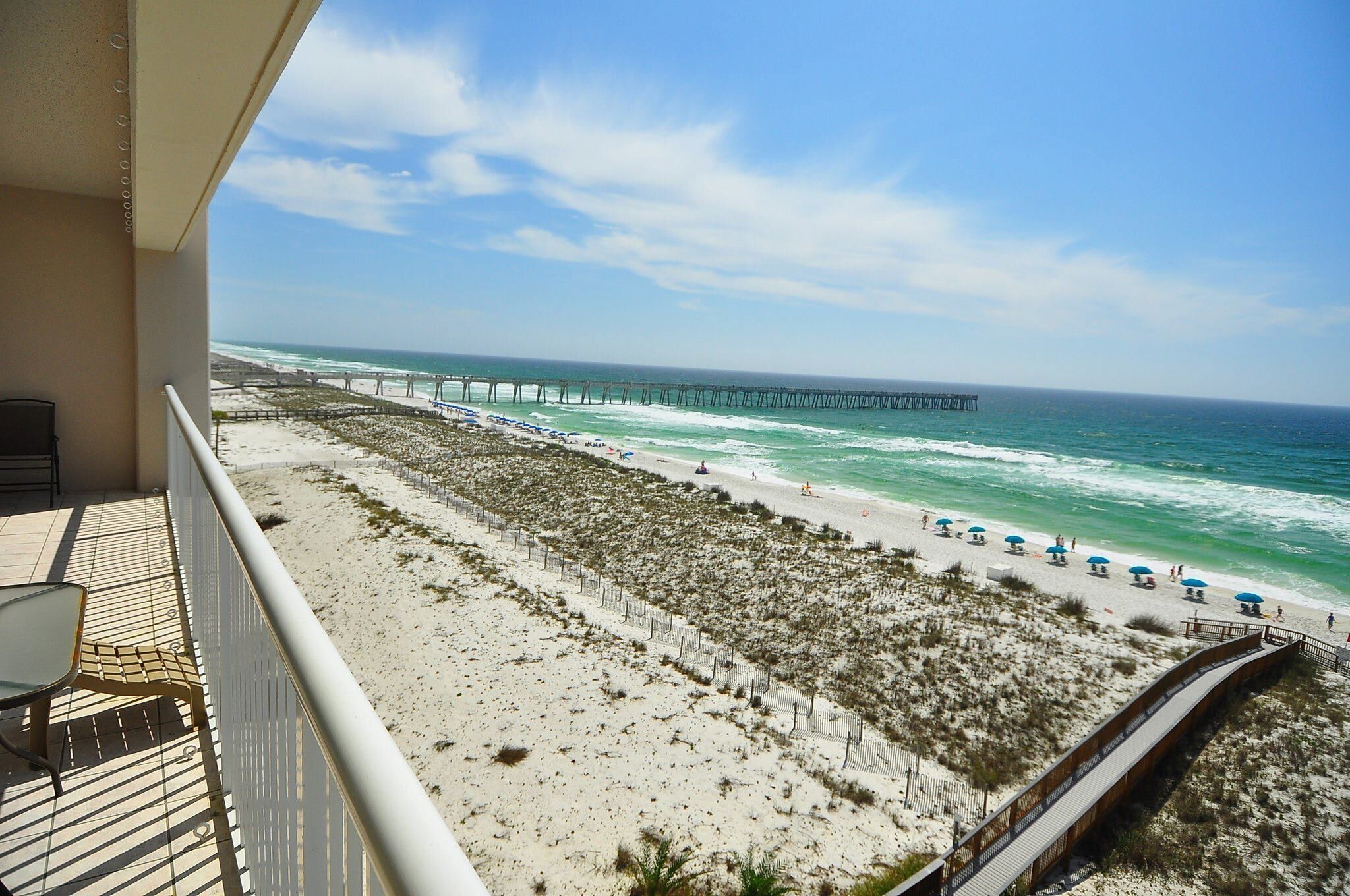A balcony with a view of a beach, a pier, and the ocean.
