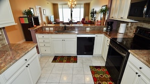 A modern kitchen with white cabinets, granite countertops, a dishwasher, an oven, and a microwave. There are two rugs on the floor.