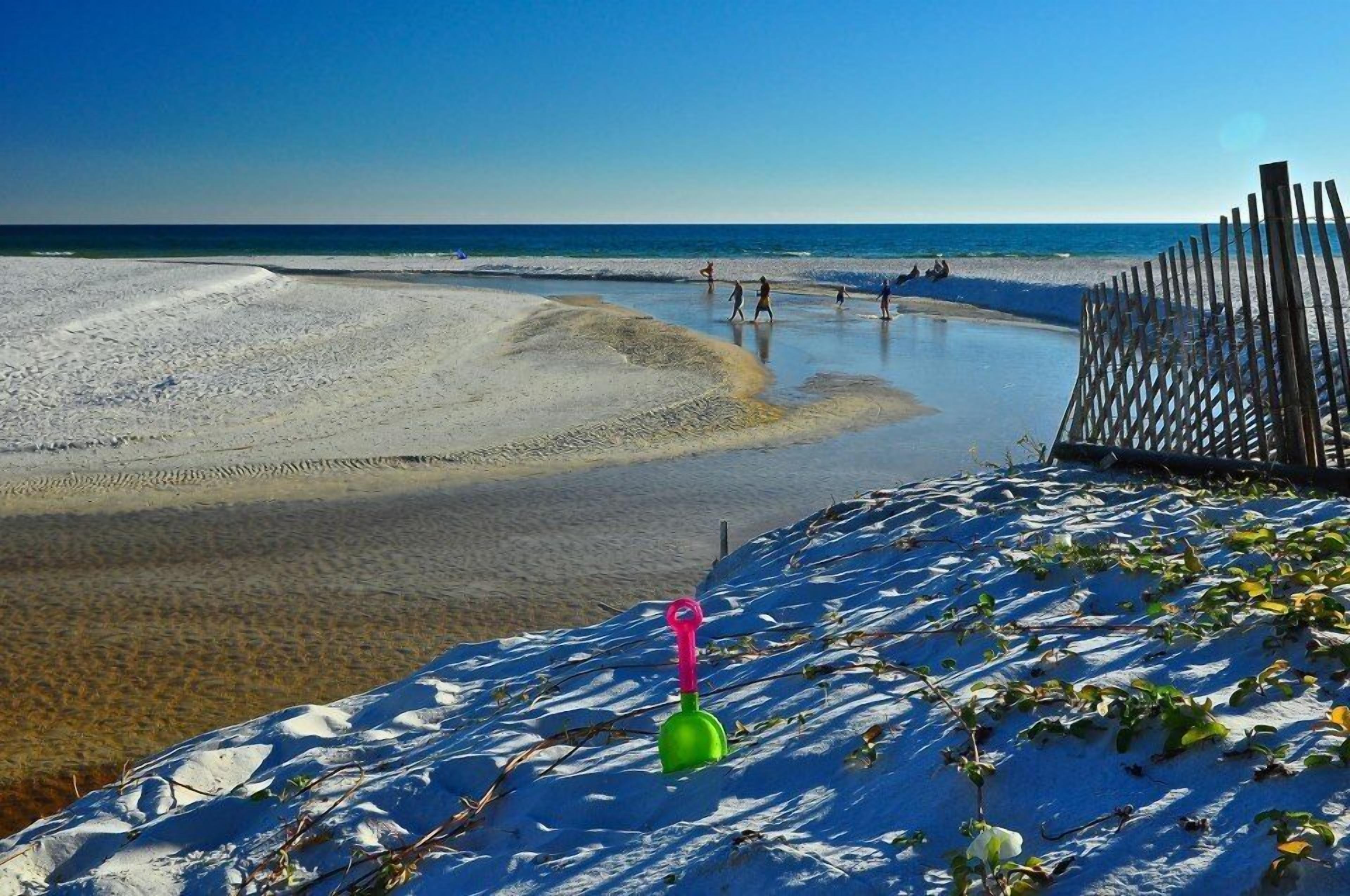 A beach with a wooden fence, clear blue sky, and a sandy area with a green shovel.