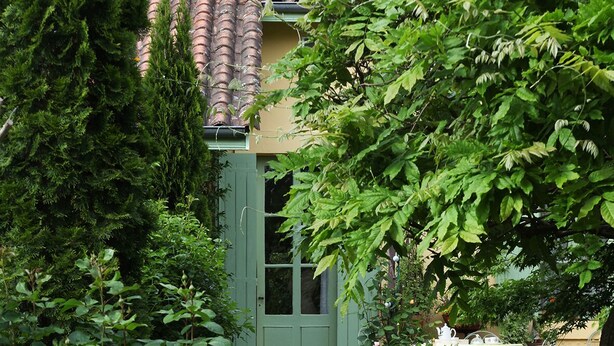 Ein Gartenweg führt zu einer grünen Tür, umgeben von  üppiger Bepflanzung und blühenden Pflanzen.