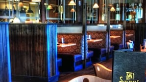 L’intérieur d’un restaurant avec des banquettes en bois, des suspensions et un panneau affichant le menu.