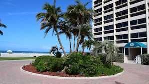 Entrada de hotel con jardín ajardinado, palmeras y vista a la playa y al océano.