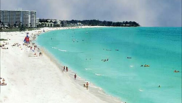 Una playa con agua turquesa cristalina, una orilla de arena y algunas personas y embarcaciones.
