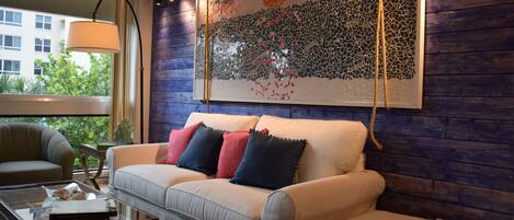 A modern living room with a sofa, a glass coffee table, and a large abstract art piece on the wall.