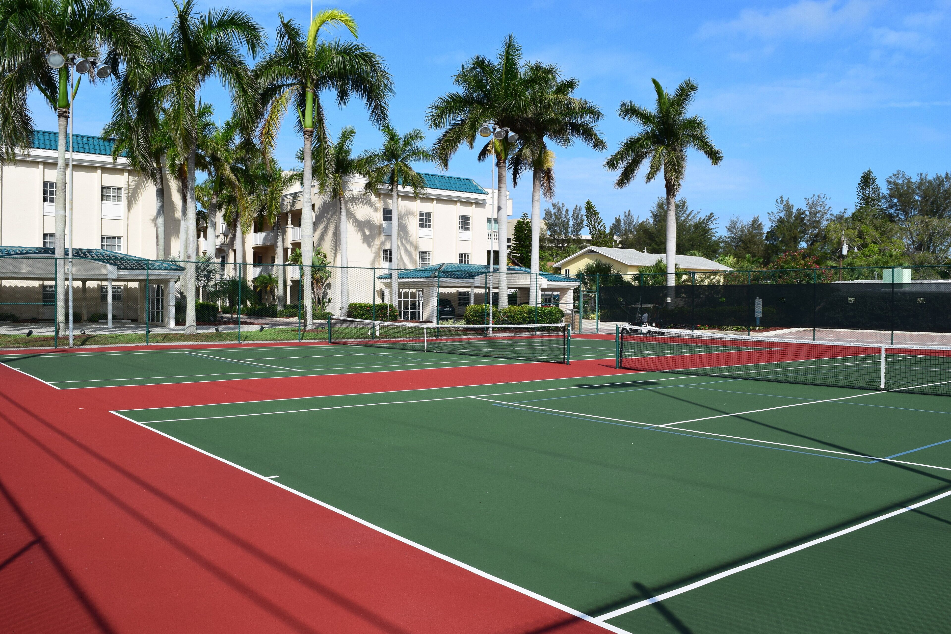 Ein Tennisplatz mit Netz, umgeben von Palmen und einem Gebäude mit grüner Dachbegrünung.