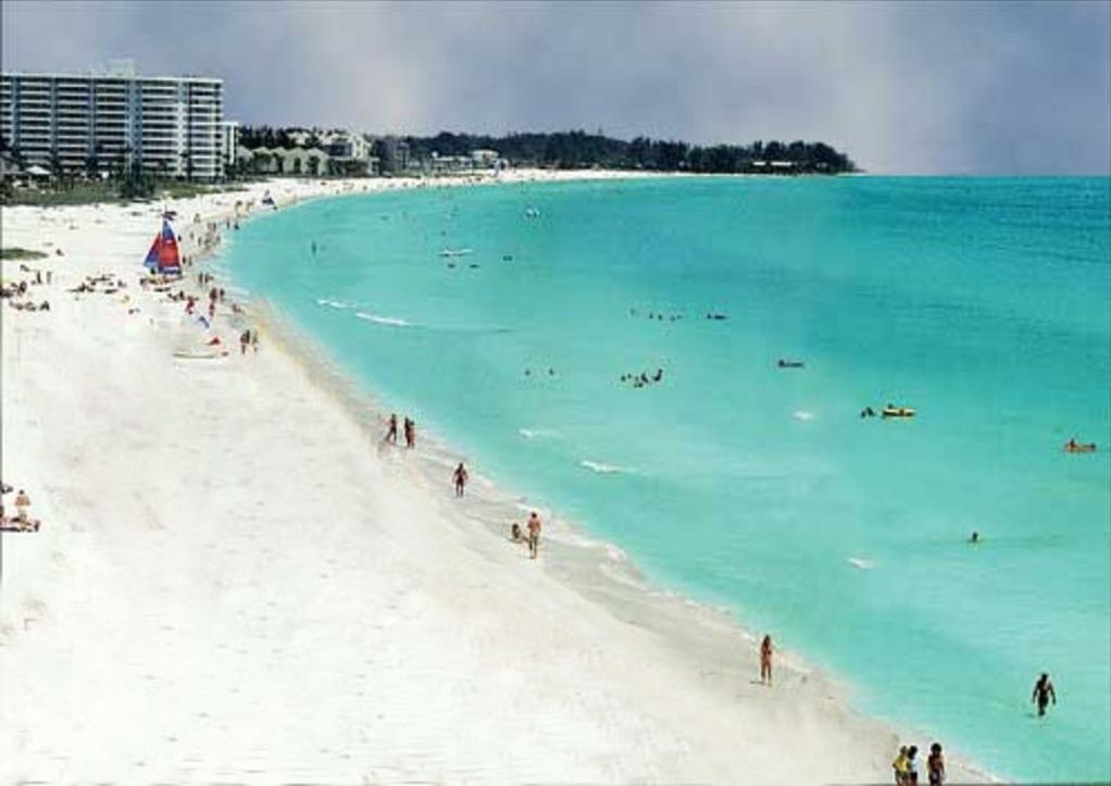 Ein Strand mit klarem türkisblauem Wasser, einem sandigen Ufer und einigen Personen sowie Booten.