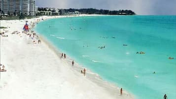 A beach with clear turquoise water, a sandy shore, and a few people and boats.