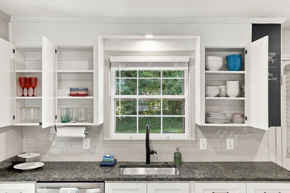 A kitchen with white cabinetry, a window with a view of greenery, a granite countertop, and a black faucet.