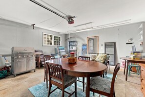A dining area with a round wooden table, chairs, and a grill.