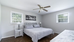 Un dormitorio con cama, mesitas de noche, ventilador de techo y un cuadro en la pared.
