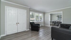 Amplia sala de estar con un gran puerta blanca, un sillón de cuero negro, un sofá de cuero negro y un comedor con mesa y sillas.
