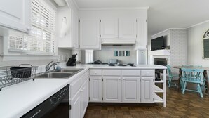 Una cocina moderna con armarios blancos, lavavajillas, pileta y comedor con mesa y sillas.