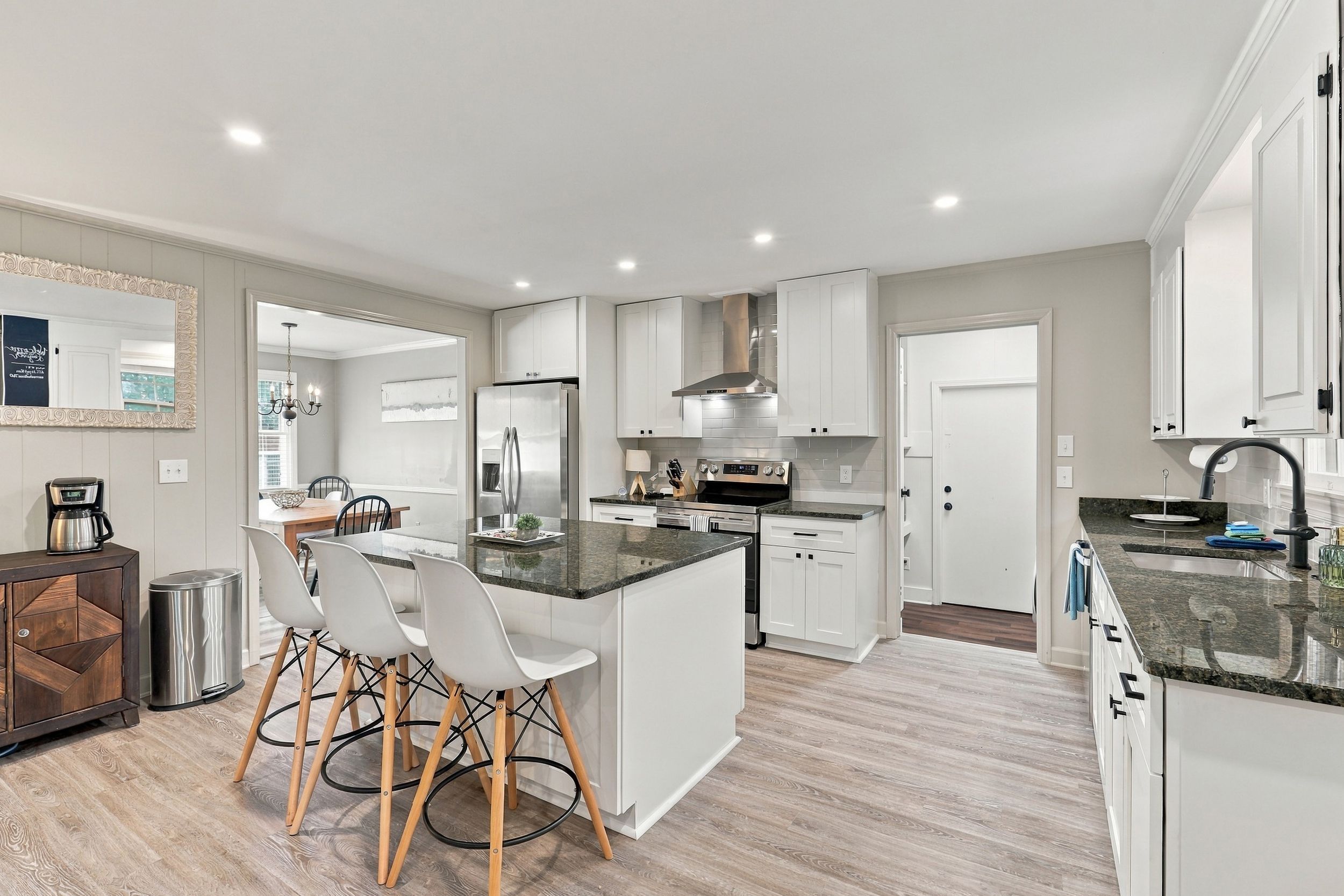 A modern kitchen with white cabinetry, a central island, and a dining area with chairs.