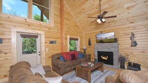 Ein gemütliches Blockhaus-Interieur mit Kamin, Ledersofas und einem Fernseher.