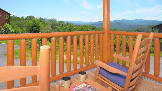 Eine Holzterrasse mit Bergblick, ein Holzstuhl mit Kissen und zwei Tassen auf einem Tisch.