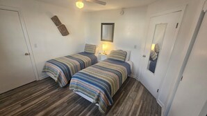 Une petite chambre propre, avec deux lits, un ventilateur de plafond et une table de chevet avec une lampe.