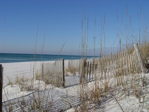 A sandy beach with a wooden fence and sparse vegetation.