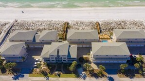 Um hotel na praia com vários edifícios, uma praia de areia e um cais.