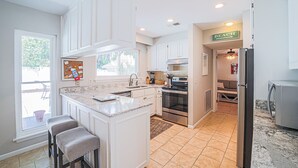 Una cocina moderna con armarios blancos, una isla grande con taburetes de bar, horno empotrado y refrigerador.
