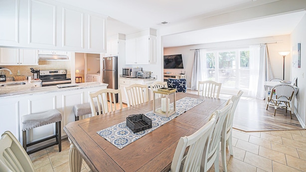 Una cocina moderna con armarios blancos, una mesa de comedor de madera y un televisor al fondo.