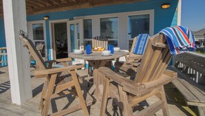 A wooden deck with a round table and chairs, a covered bench, and a view of the ocean.