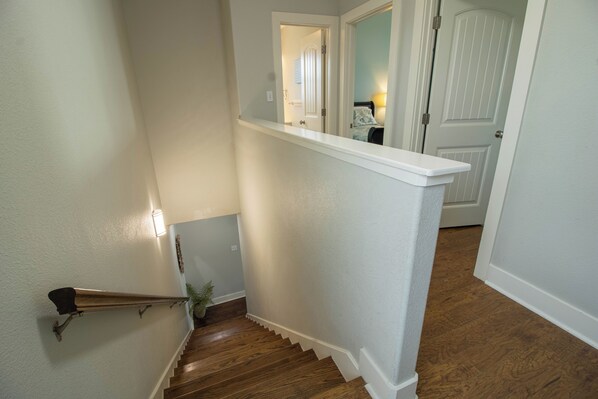 A staircase with wooden steps and white walls, leading to a room with a bed and a nightstand.