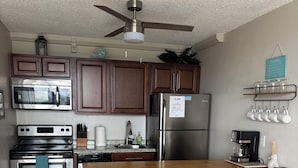 A modern kitchen with stainless steel appliances, wooden cabinets, and a bar area with stools. - Beautiful condo on the Beach with Heated Pool, Pickleball, free WiFi & parking! (Fort Myers Beach)