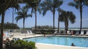 A swimming pool with lounge chairs and palm trees, overlooking a beach. - Beautiful condo on the Beach with Heated Pool, Pickleball, free WiFi & parking! (Fort Myers Beach)