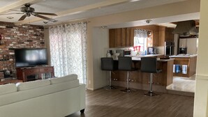 Un soggiorno moderno con divano, televisore e angolo cottura con pensili in legno e uno sgabello da bar.