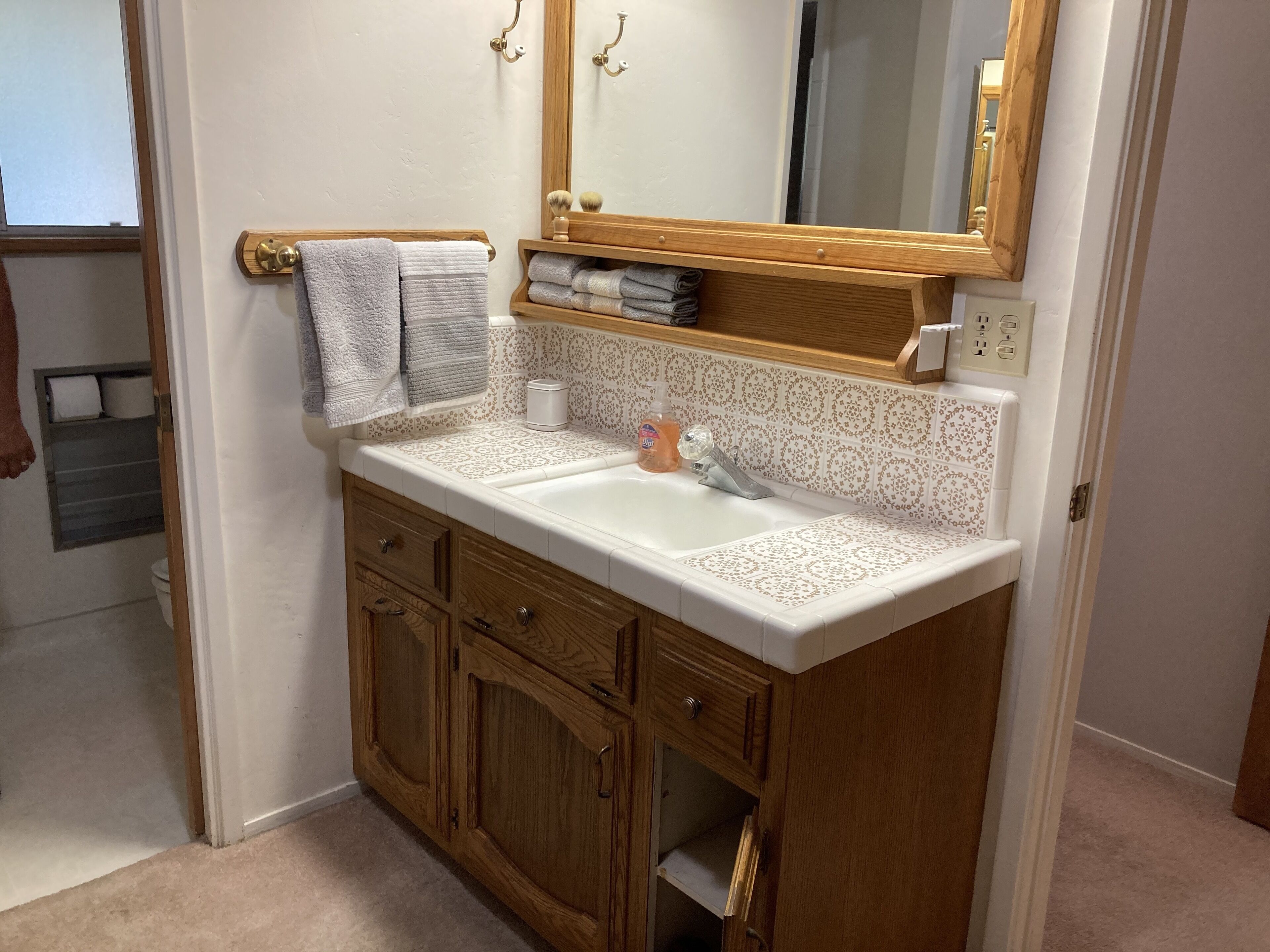 Une salle de bain avec un meuble-lavabo en bois, un évier et un miroir. Des serviettes sont suspendues sur un porte-serviettes et une étagère contient des articles de toilette.