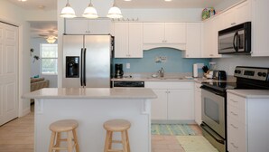 A modern kitchen with white cabinets, a central island with stools, a microwave, a stove, and a coffee maker.