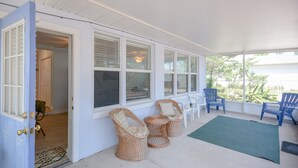 A covered porch with wicker chairs, a small table, and a view of the outdoors.