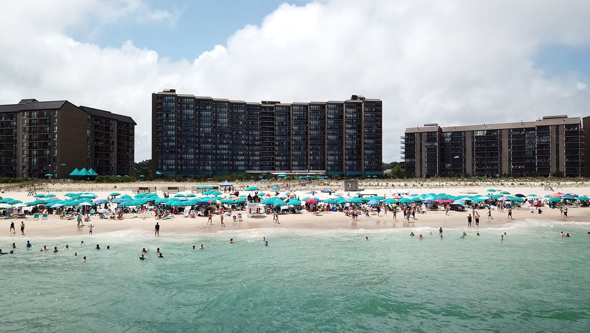 A beachfront hotel with multiple floors, a sandy beach, and numerous umbrellas.