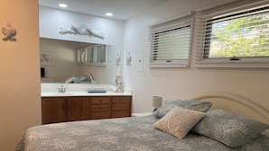 A bedroom with a bed, a nightstand, a window with blinds, and a bathroom visible through an open door. - Sea Colony West - 2BR, 2BA - 1 Block to Tennis Center, 1/2 Mile to Beach (Bethany Beach)