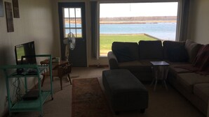 A living room with a large window overlooking a body of water, a sofa, a television, and a small table.