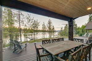 Een houten terras met een tafel en stoelen, uitkijkend op een meer omringd door bomen.