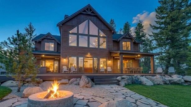 Une grande maison en bois avec un foyer extérieur, un espace salon de jardin et un chemin en pierre.