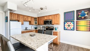 Cocina moderna con armarios de madera, encimera de granito y electrodomésticos de acero inoxidable. Hay cuatro cuadros en la pared.