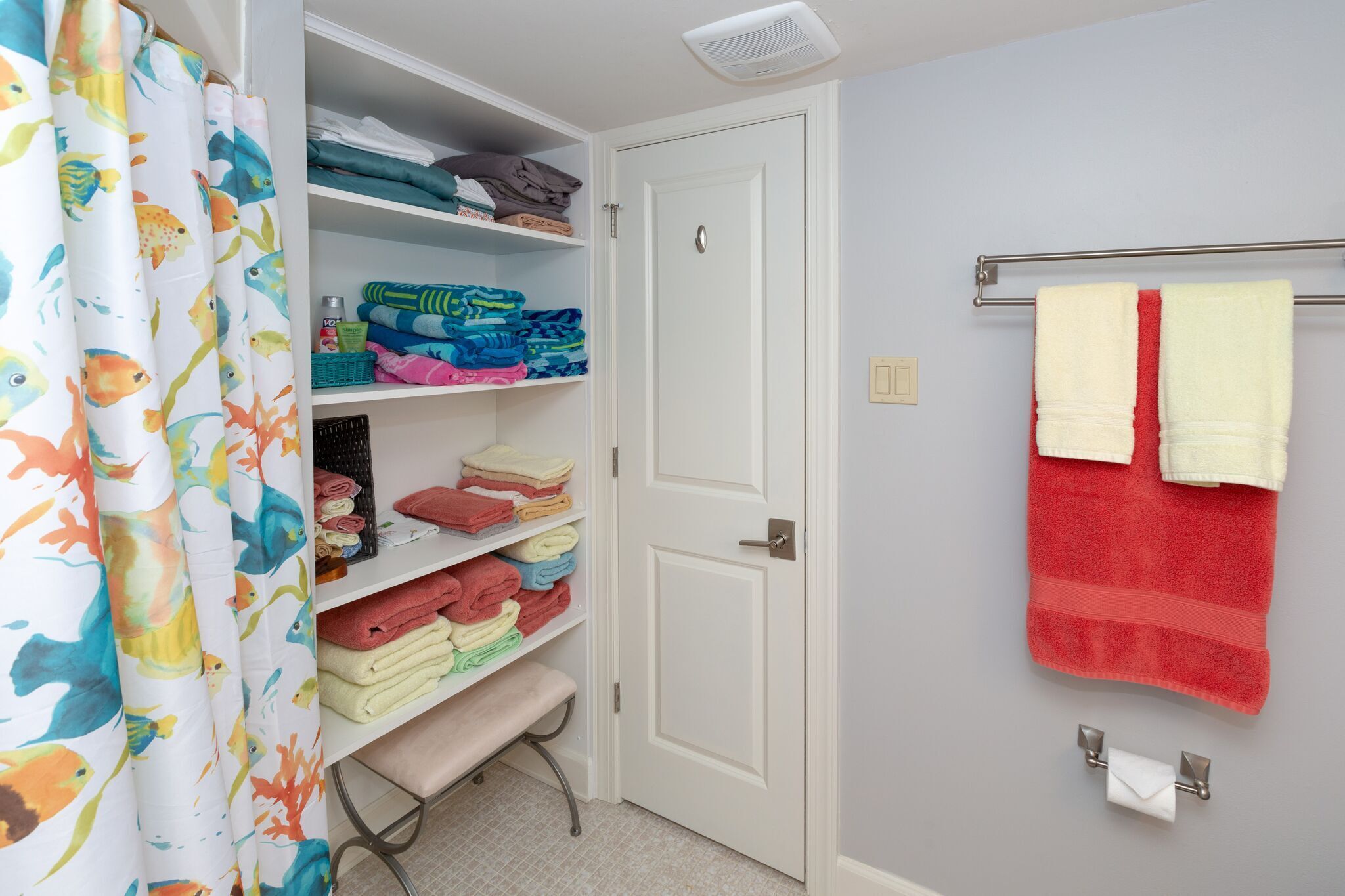 A bathroom with a shower curtain, shelves with folded towels, a towel rack, and a toilet paper holder.