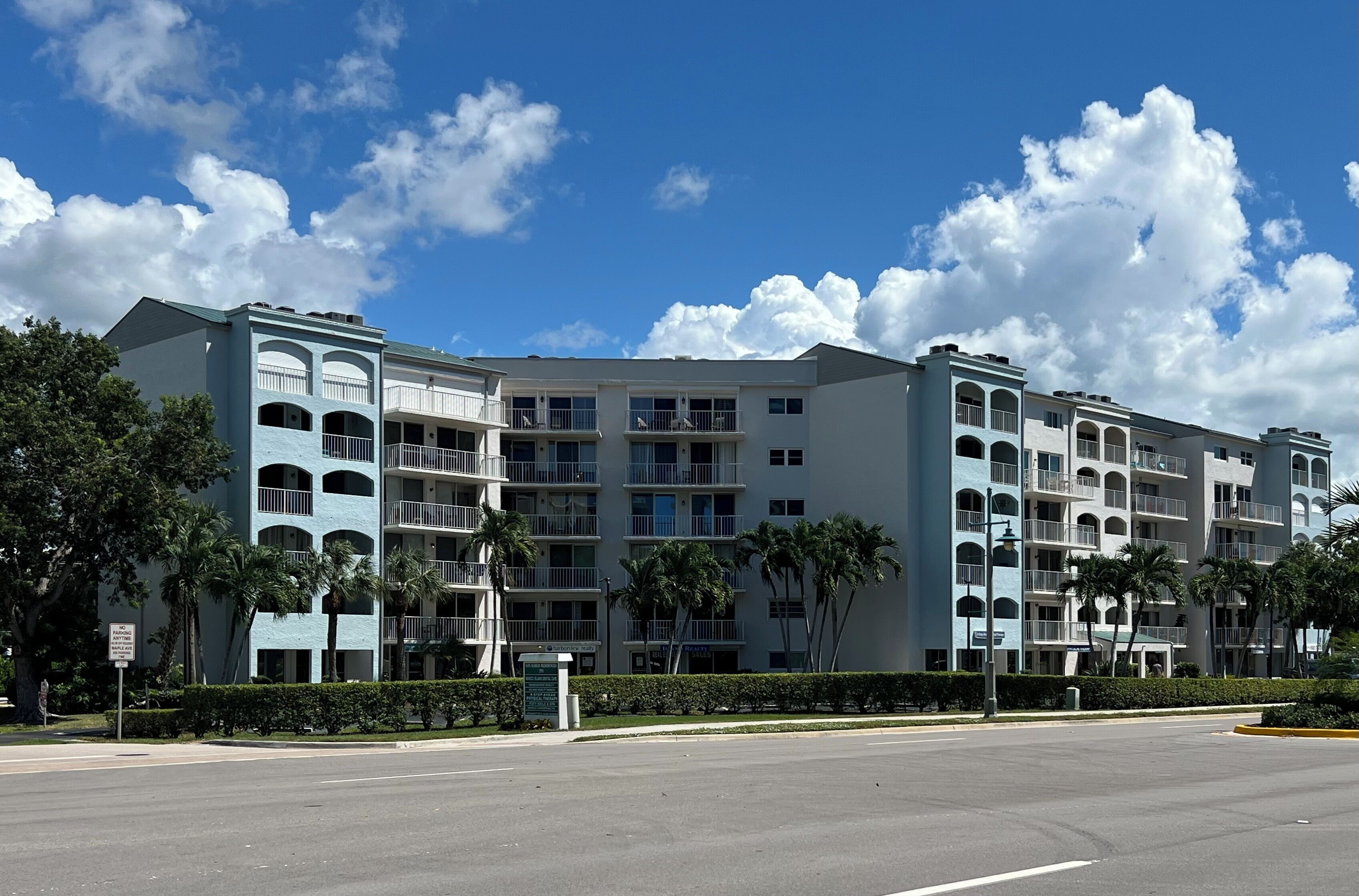 Un hotel de varios pisos con balcones, palmeras y un cielo azul despejado.
