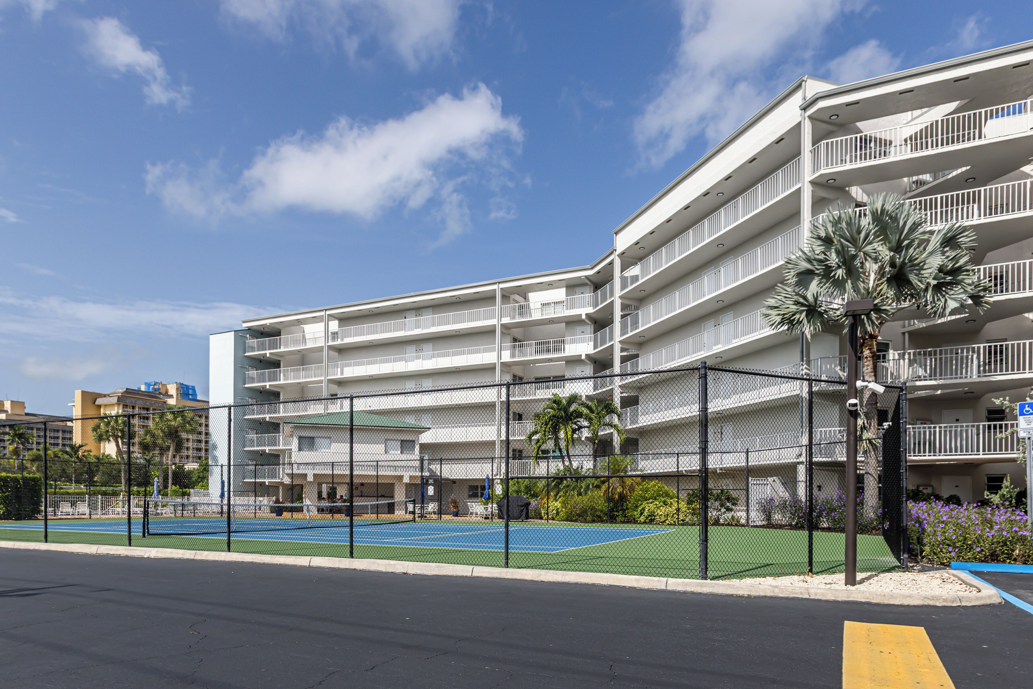 A multi-story hotel with balconies, a fenced tennis court, and a clear sky.