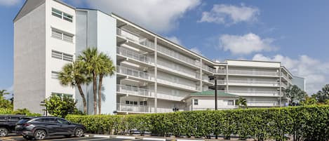 Un hotel de varios pisos con fachada blanca, balcones y un estacionamiento con espacios reservados.